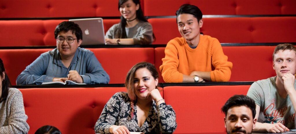 Six students sat in lecture theatre facing front and smiling
